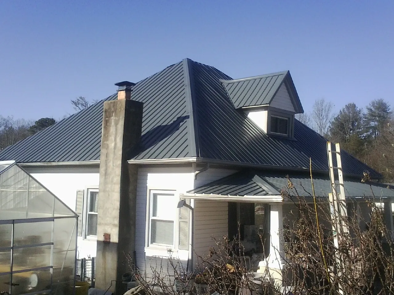 Dark blue standing seam metal roof on a white farmhouse with dormer — Slate & Tile Roof Repair by Roofing Brothers in Lacon