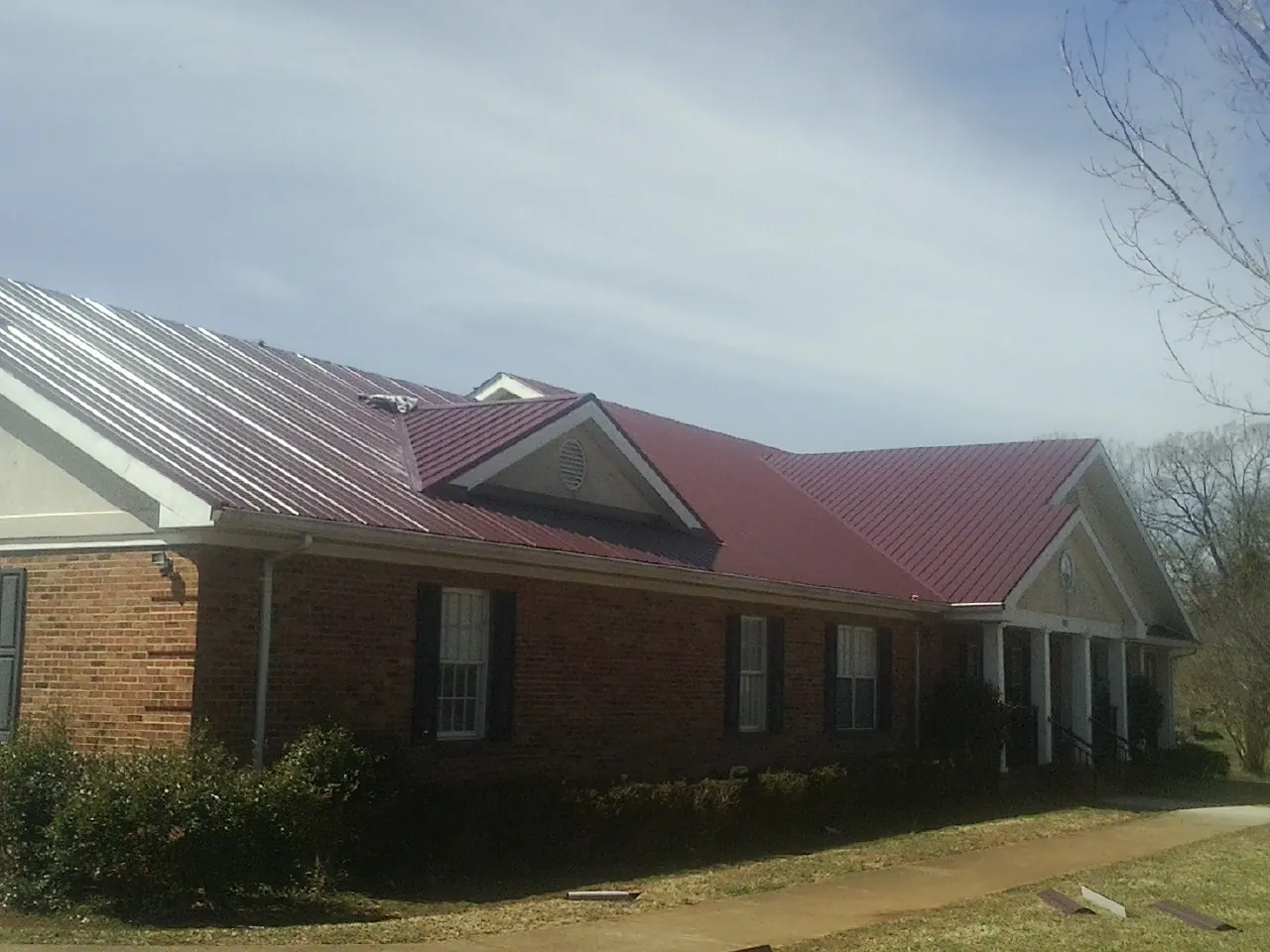 Red metal roof with gabled entries on a long brick building, from a Hail Damage Roof Repair job in Lacon