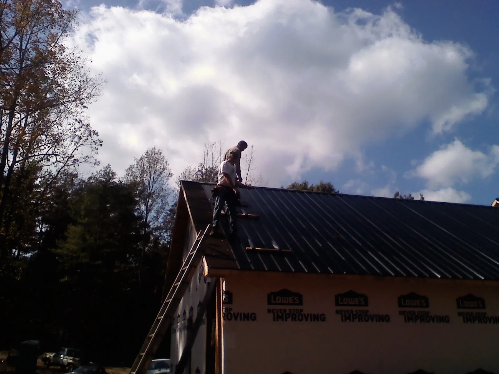 Roofer fastening dark metal panels high against a cloudy sky, from a Roof Inspection job in Lacon